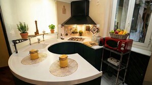 A modern kitchen with a curved island, a black range hood, and a fruit basket on the window sill. - Navona Apartment (Rome)