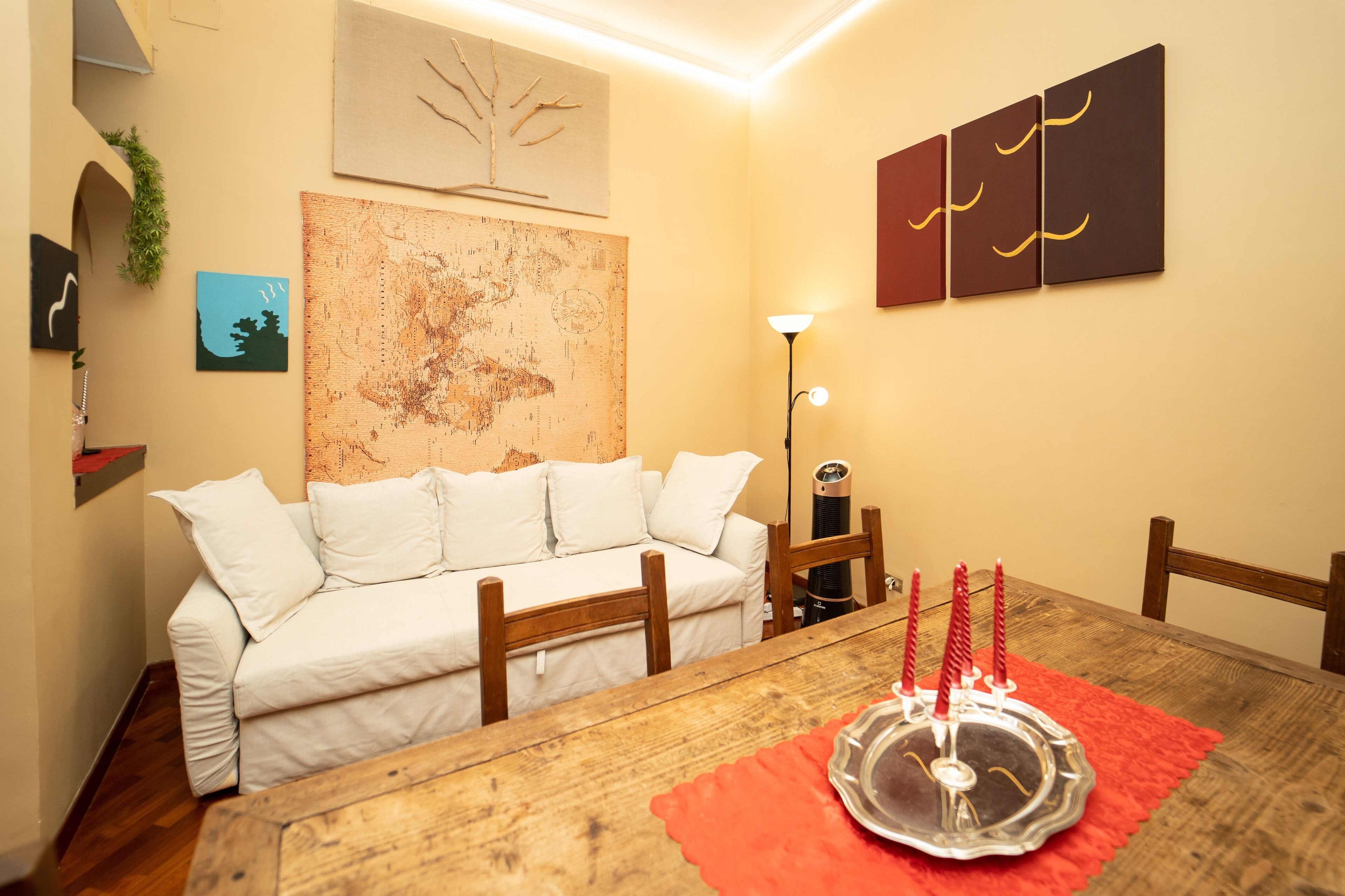 A cozy room with a wooden dining table, a white sofa, a map on the wall, and a lamp.