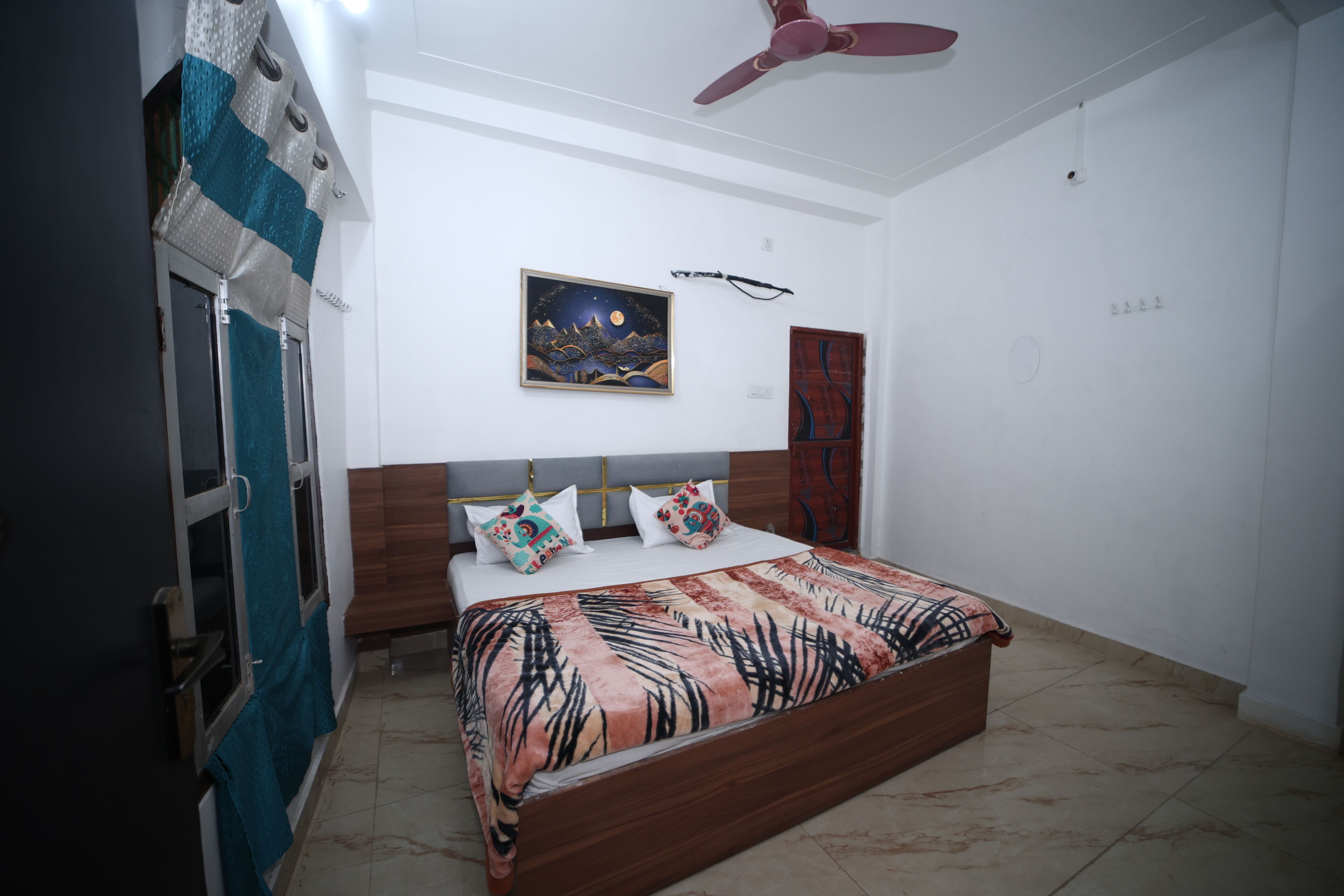 A bedroom with a bed, a ceiling fan, a night sky painting, and a wooden wardrobe.