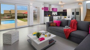 A modern living room with a grey sofa, white coffee table, and a glass sliding door leading to a pool. - Modern villa with pool, garden and sea view for 8 people in Istria (Galižana)
