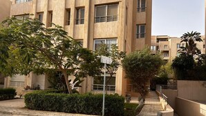 Edificio residenziale con cortile pavimentato, circondato dal verde e da un cielo sereno.