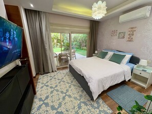 A bedroom with a large bed, a TV, a sliding glass door to a patio, and a ceiling light. - Top rated 1 BR+private garden in compound - families & single travelers only (Giza Governorate)