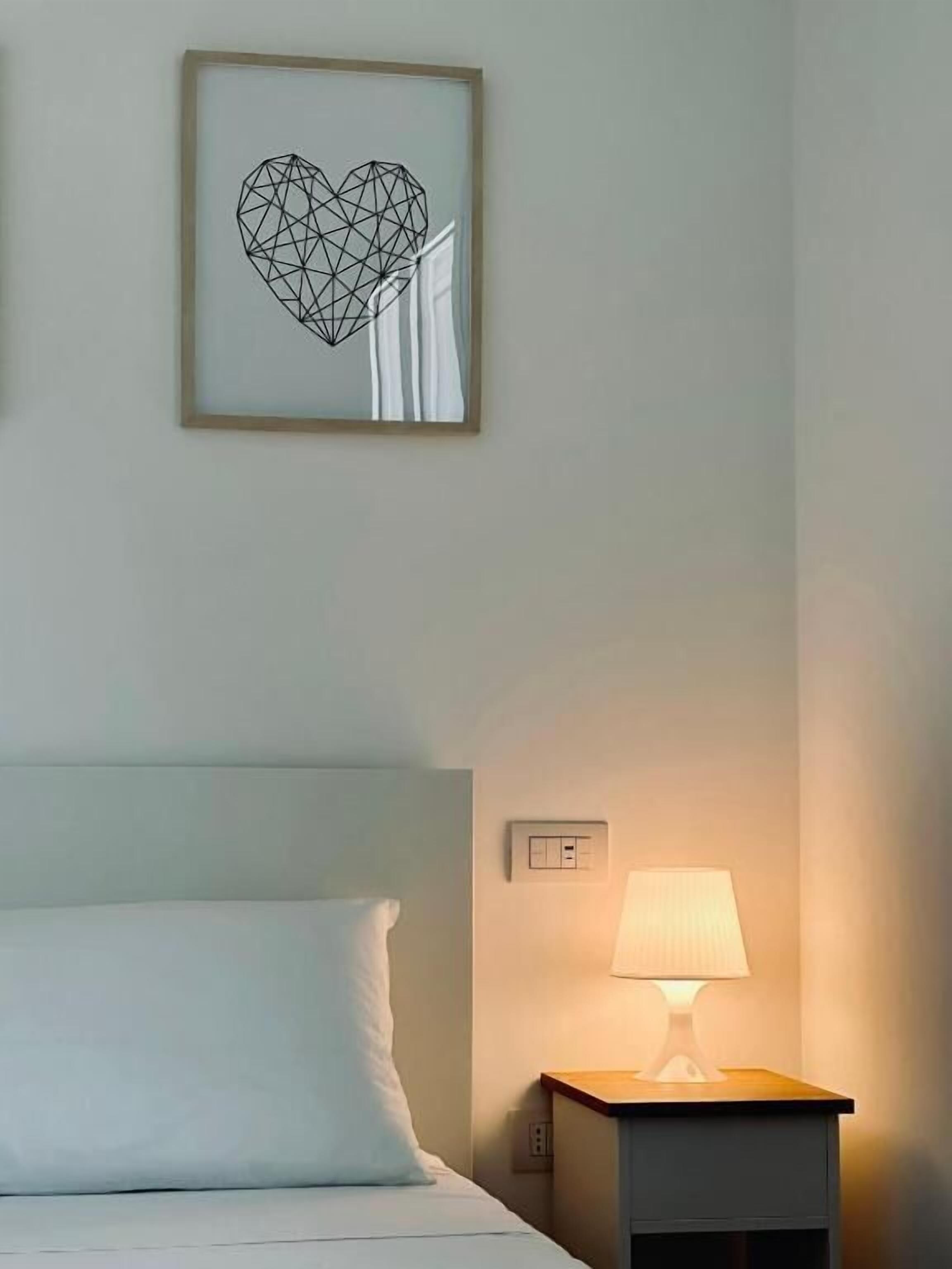 Una camera d'albergo con un letto, un comodino con una lampada e un quadro geometrico appeso alla parete.