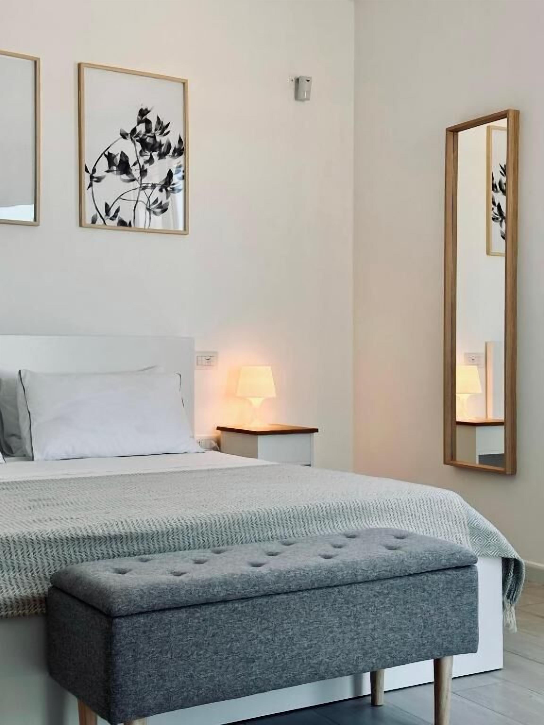 Un dormitorio con cama, mesitas de noche, lámpara, espejo y cuadros en la pared.
