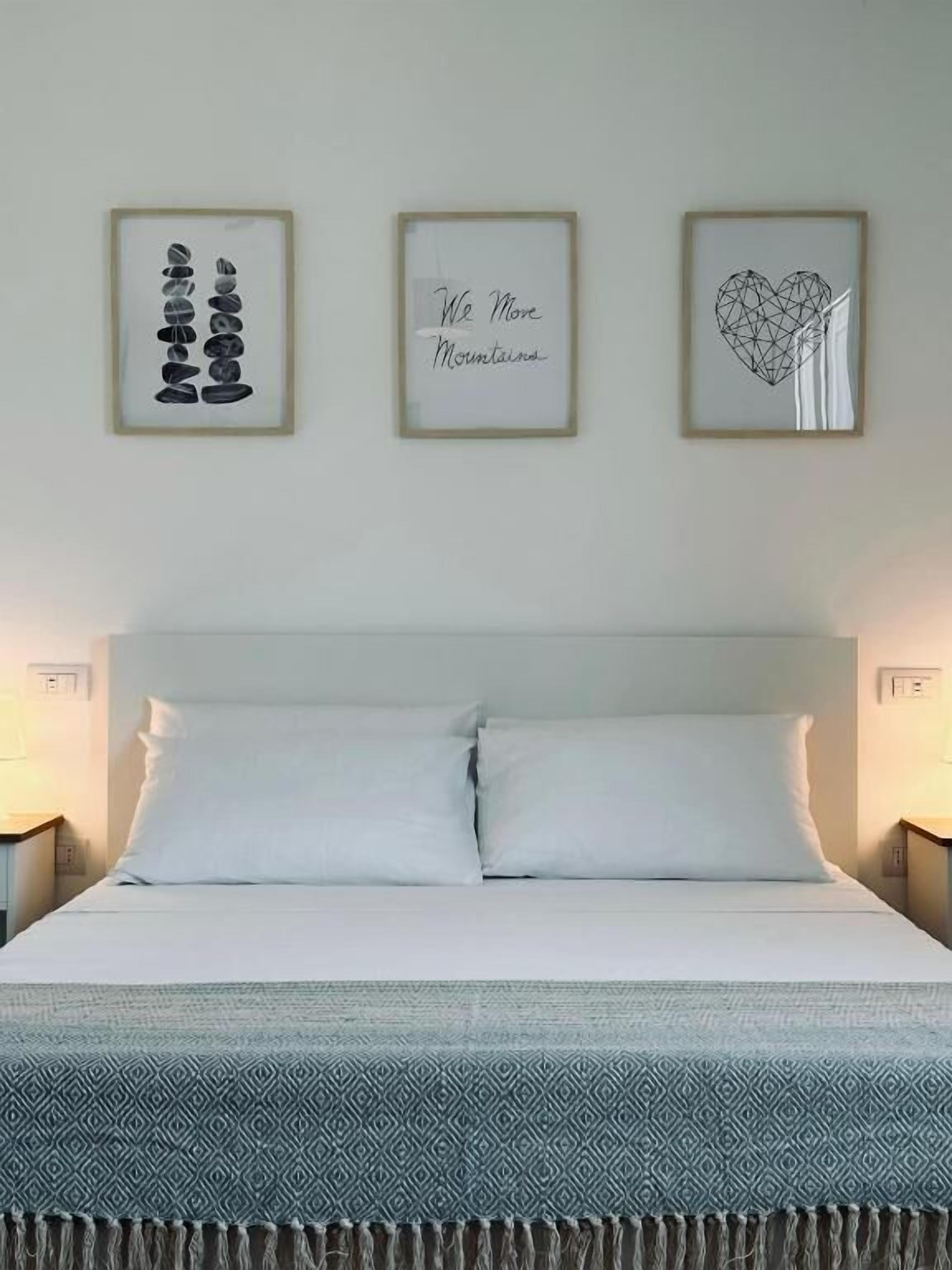 Een bed met witte lakens, een gestreepte plaid en drie ingelijste kunstwerken aan de muur erboven.