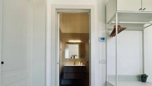 A hallway leading to a bathroom with a mirror, sink, and towel rack. - Villa Noga Rooms (Selargius)