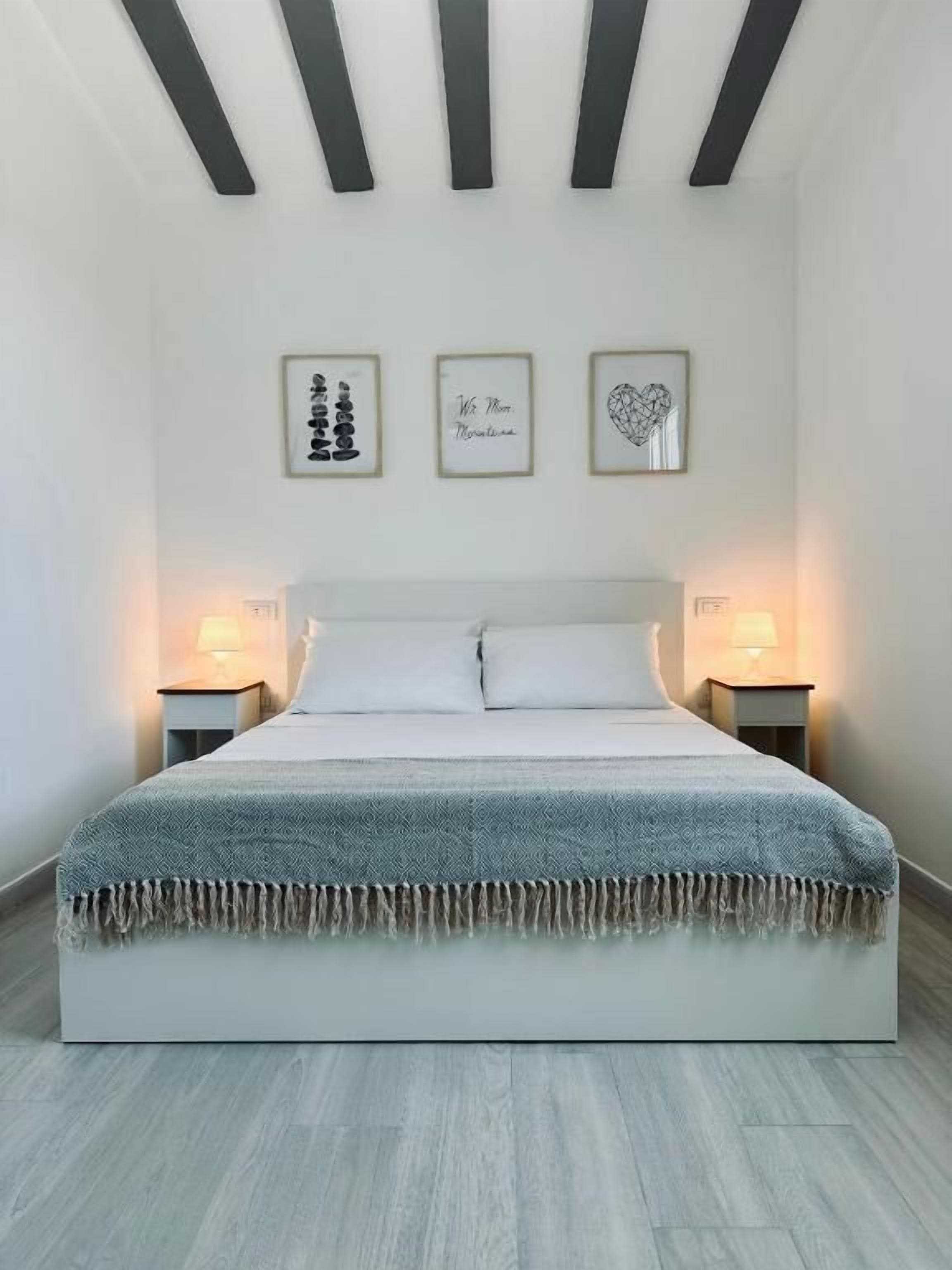 Une chambre à coucher comprenant un lit, deux tables de chevet et trois œuvres d’art encadrées accrochées au mur.