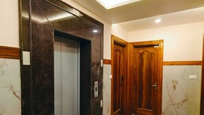 Un pasillo con piso de mármol, una puerta de madera y un moderno ascensor con acabado metálico.