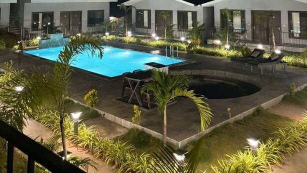 A nighttime view of a hotel with a swimming pool, outdoor seating, and well-lit pathways.