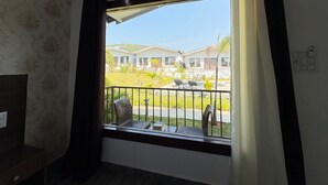 A room with a balcony, a view of houses, and a window with curtains.