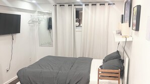 A bedroom with a bed, a wooden table, a chair, a TV, a mirror, and a window with curtains. - Delightful Studio in Montréal perfect for your city getaway (Montréal)