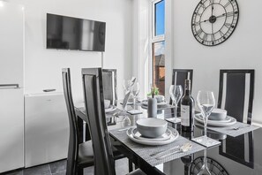 Ein moderner Essbereich mit einem Tisch für vier Personen, einem an der Wand befestigten Fernseher und einer großen Wanduhr.
