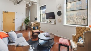 Un salon moderne doté d’une grande fenêtre, d’un téléviseur à écran plat et de différents types de sièges, notamment un canapé, des fauteuils et une table basse.