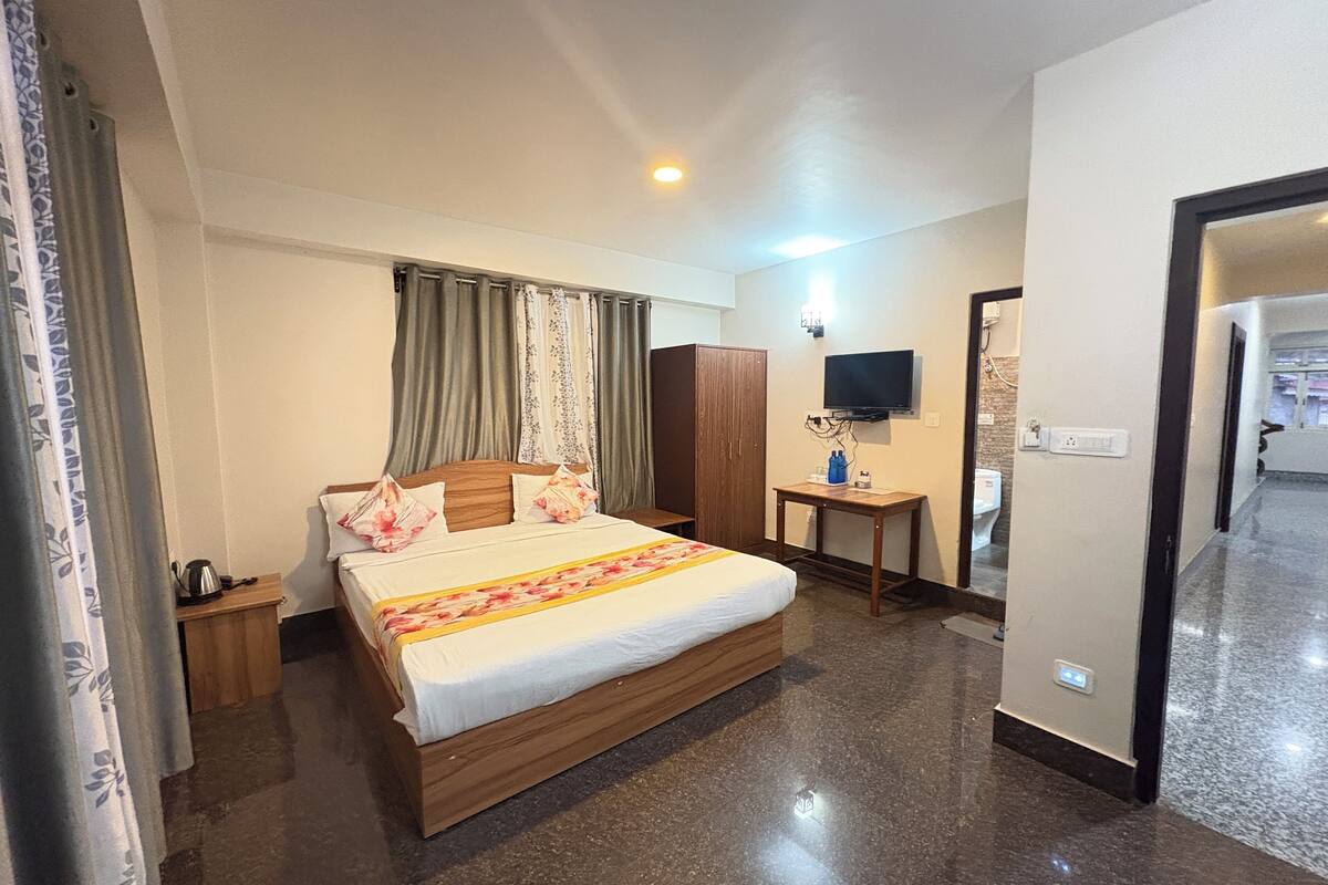 A hotel room with a wooden bed, a television on the wall, a small table, and a wardrobe.