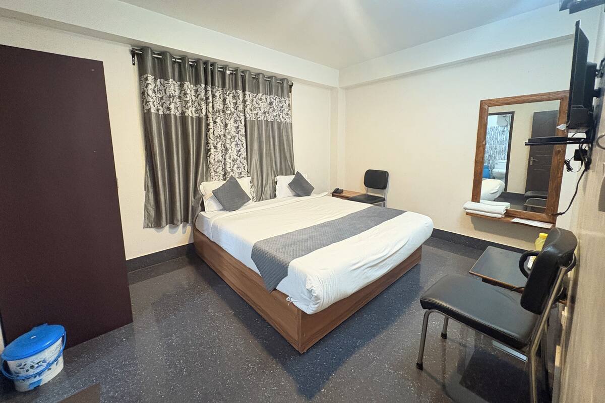 A hotel room with a bed, a desk, a chair, a mirror, and a window with curtains.
