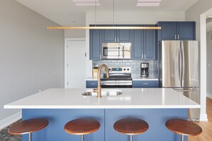 A modern kitchen with blue cabinets, a stainless steel refrigerator, a central island with stools, and a built-in oven. - Live Artfully in This 2BR Stay (Philadelphia)