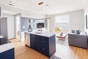 A modern kitchen with a central island, a built-in dishwasher, and a large window offering a city view. - Live Artfully in This 2BR Stay (Philadelphia)