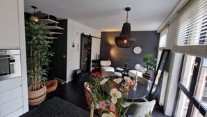 Una sala moderna con comedor, un ventanal con persianas, una lámpara decorativa y una planta en maceta.