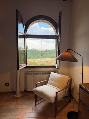 Ein Zimmer mit einem großen Bogenfenster, einem Sessel, einer Stehlampe und einer Heizung.