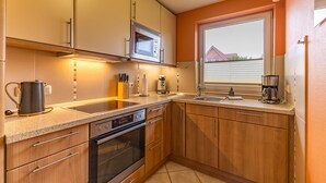 Une cuisine compacte équipée d’un four à micro-ondes, d’une cuisinière et d’une machine à café, avec des meubles en bois et une fenêtre donnant sur une maison.