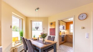 Un coin repas comprenant une table, des chaises, un vase avec des fleurs et donnant sur la cuisine.