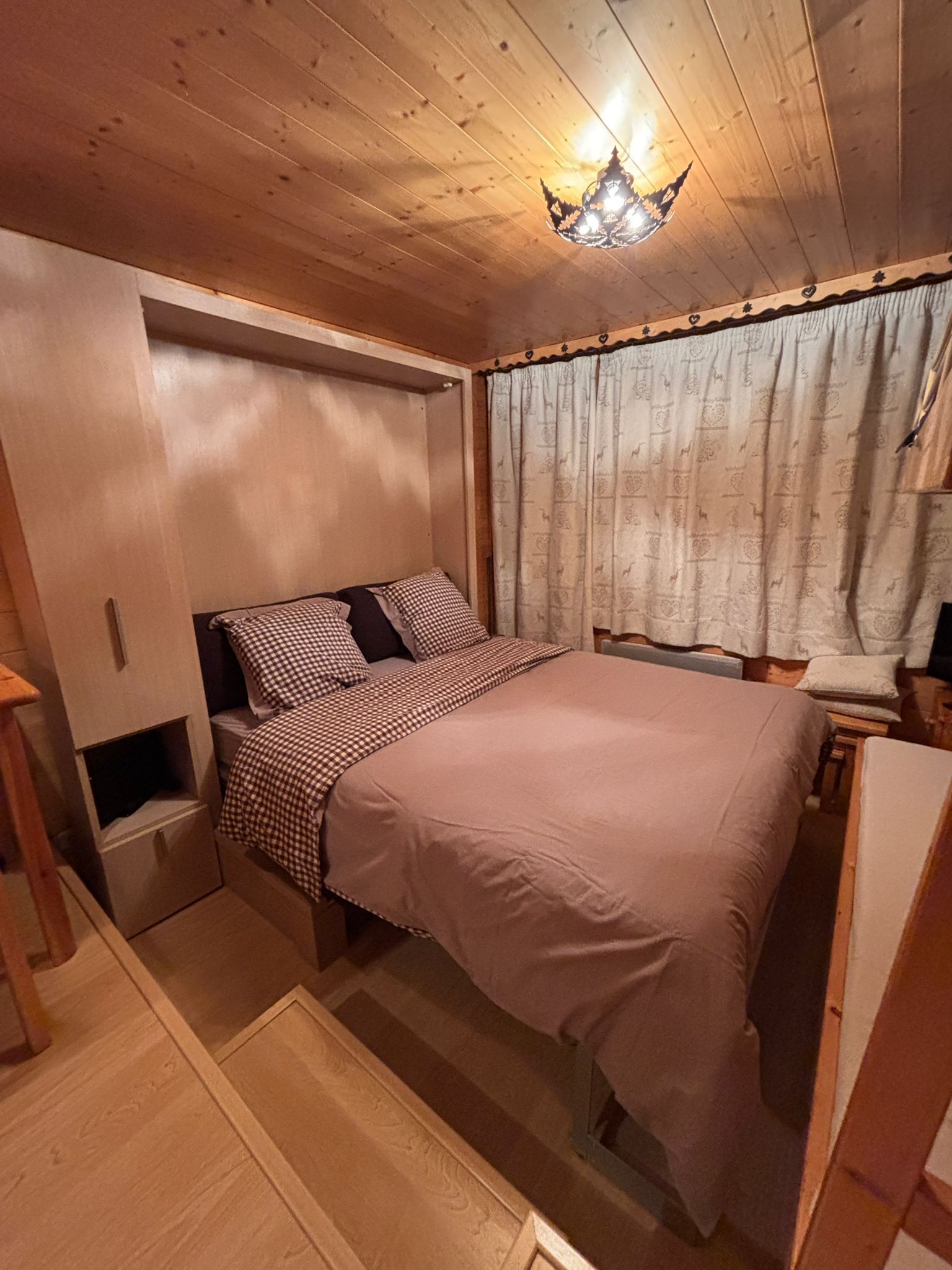 Een gezellig slaapkamer met een bed, nachtkastje, dressoir en een raam met gordijnen.
