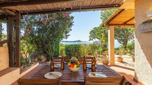 An outdoor dining area with a table set for two, surrounded by potted plants and a view of the sea. - Wonderful private villa for 4 guests (Villasimius)