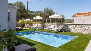Ein Swimmingpool mit Liegestühlen und Sonnenschirmen, umgeben von einer Steinmauer und Grünpflanzen.