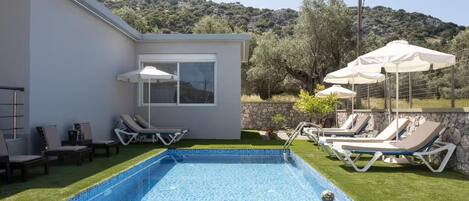 A modern pool area with a rectangular pool, lounge chairs, and umbrellas.