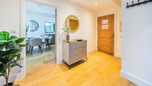 A hallway with a wooden floor, a grey cabinet with drawers, a mirror with a gold frame, and a door with a 'NO NOISE POLICY' sign.