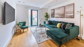 A modern living room with a green sofa, a small round coffee table, and a TV mounted on the wall.