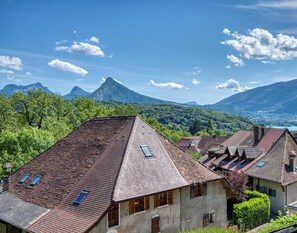 Ein traditionelles europäisches Dorf mit terrakottafarbenen Dächern, einem markanten Berg im Hintergrund und üppiger Vegetation.