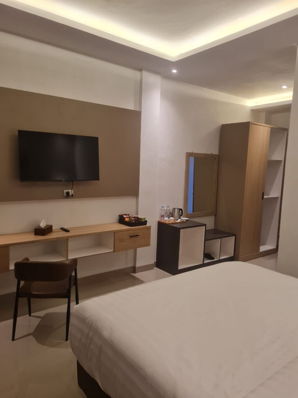 Habitación de hotel moderna con una cama grande, un escritorio con televisión de pantalla plana, un armario y un espejo.