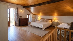A bedroom with a wooden ceiling, a large bed, two bedside tables with lamps, a dresser, and a window with curtains.