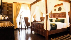 Uma cama de dossel com cortina, uma escrivaninha de madeira, uma cadeira e um tripé em um quarto com piso e paredes de madeira escura.
