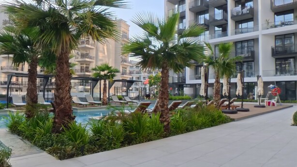 A modern hotel with a pool area, palm trees, and sun loungers. - Beverly Boulevard By HMB HOMES (Dubai)