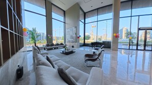 A spacious lobby with a large sofa, armchairs, and a piano, featuring large windows with a city view. - Beverly Boulevard By HMB HOMES (Dubai)