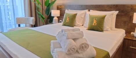 A neatly made bed with green and white bedding, two pillows with the letter 'B', and a stack of folded white towels.