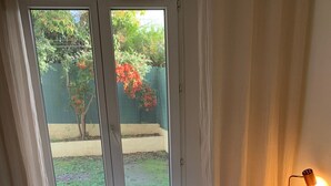 Ein Schlafzimmer mit einem Bett, einem Nachttisch, einer Lampe und Blick auf einen Garten durch eine Schiebetür.