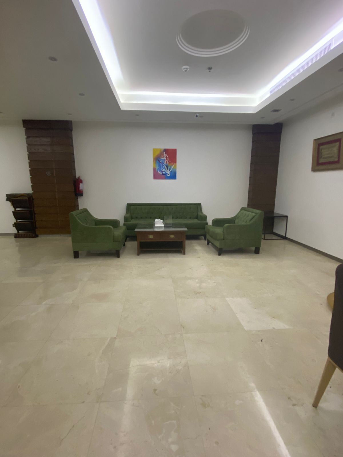 Een ruime lobby met een groene zitbank, een klein houten tafeltje en een kleurrijk abstract schilderij aan de muur.
