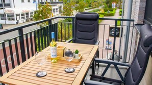 A balcony with a wooden table, two chairs, a bottle of Michel Soudier wine, and a glass. - Coastal berth - KÜSTE33/14 - Sauna. Balcony. Family-friendly. (Tossens)