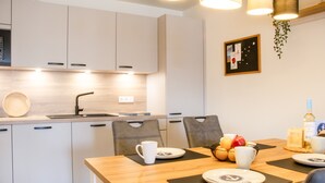 A modern kitchen with white cabinets, a wooden dining table, and a hanging plant. - Coastal berth - KÜSTE33/14 - Sauna. Balcony. Family-friendly. (Tossens)