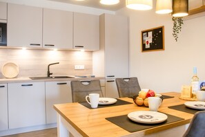 A modern kitchen with white cabinets, a wooden dining table, and a hanging plant. - Coastal berth - KÜSTE33/14 - Sauna. Balcony. Family-friendly. (Tossens)