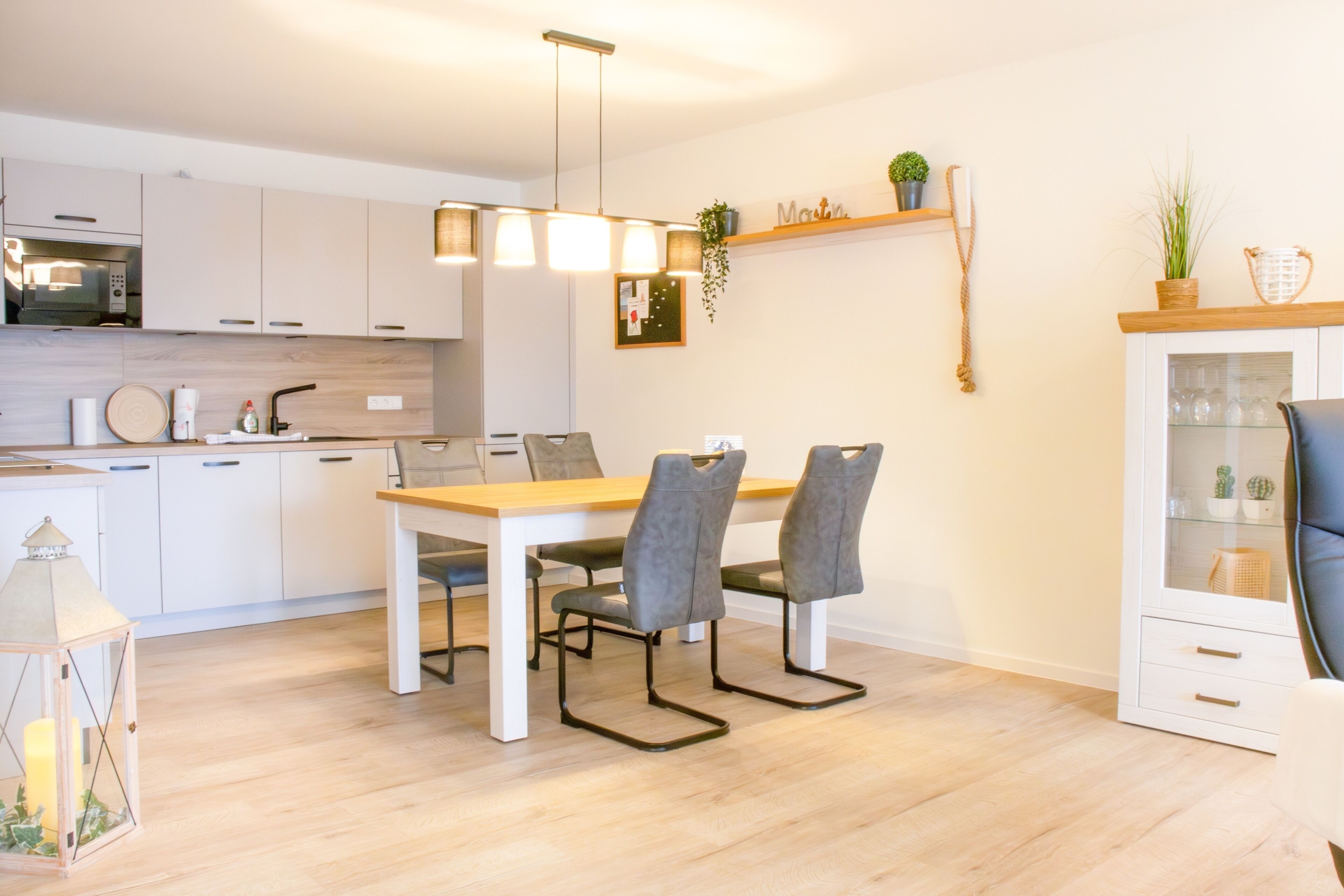 A modern kitchen with white cabinets, a wooden dining table, and grey chairs.