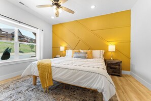A bedroom with a bed, bedside lamps, a window, and a view of a house.