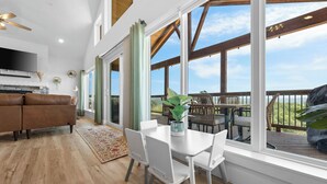 Amplia sala de estar con un ventanal que da a una terraza, una mesa de comedor blanca y un sofá de cuero marrón.