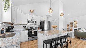 Una cocina moderna con armarios blancos, electrodomésticos de acero inoxidable y una isla central con taburetes de bar.