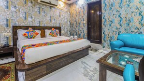 A bedroom with a bed, a blue sofa, a glass coffee table, and patterned wallpaper. - Anand Hotel With banquet hall Karol Bagh (New Delhi)