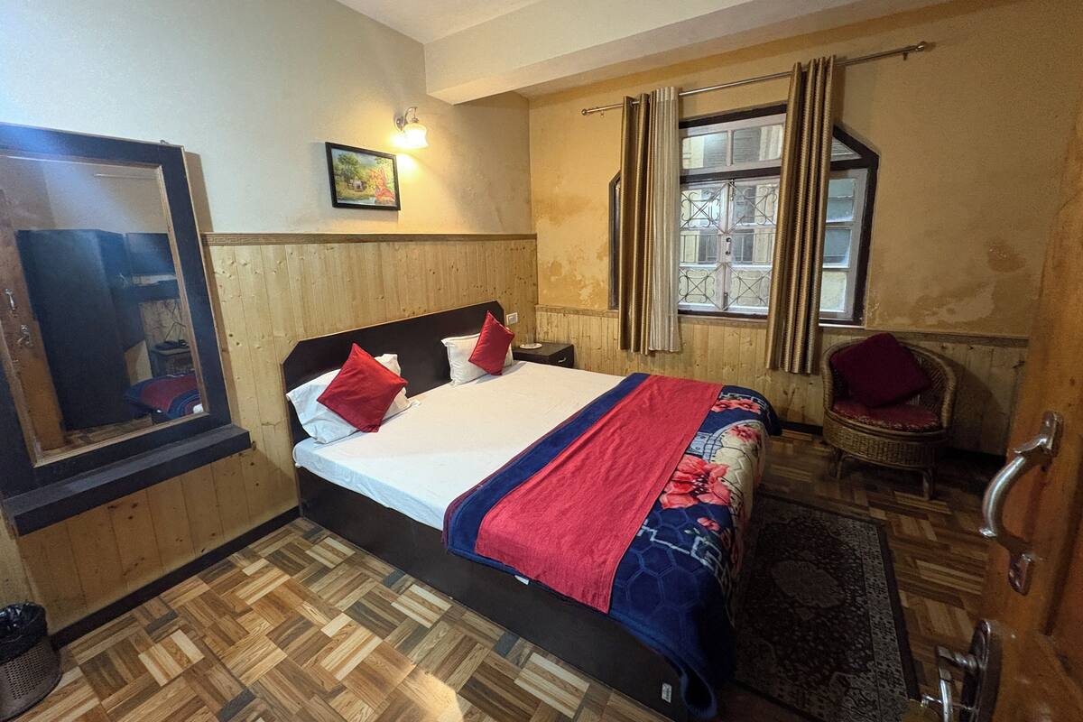 Ein Schlafzimmer mit Holzboden, einem Bett mit rot-weiß gestreifter Bettwäsche, einem Sessel, einem Fenster mit Vorhängen und einer Wandleuchte.