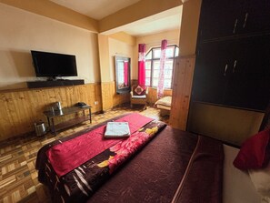 Une chambre avec un lit, un téléviseur fixé au mur, une fenêtre avec des rideaux et une armoire.